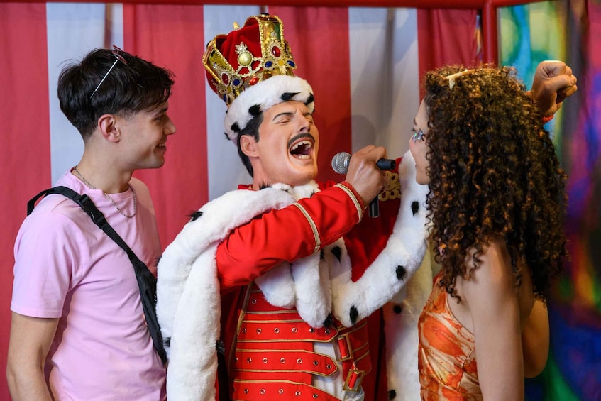 A person in a red and white costume with a crown, holding a microphone and interacting with two other people. 4