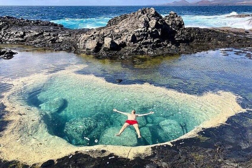 A person in a red swimsuit floating in a clear blue water body surrounded by rocky terrain. 3