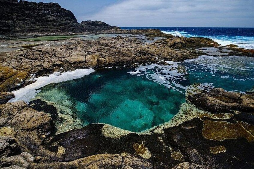 A rocky coastline with clear turquoise waters and a small inlet surrounded by rugged terrain. 1