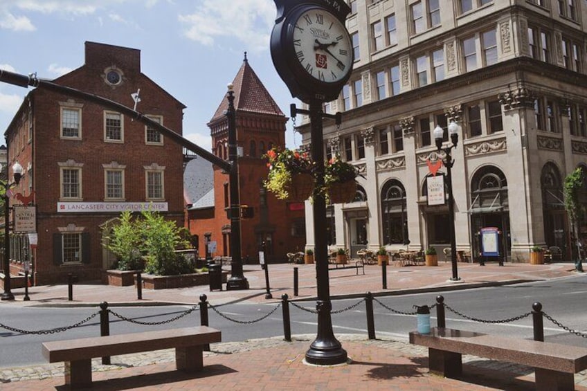 A clock, a bench, and a building with a sign that reads "Lancaster City Visitor Center". 2