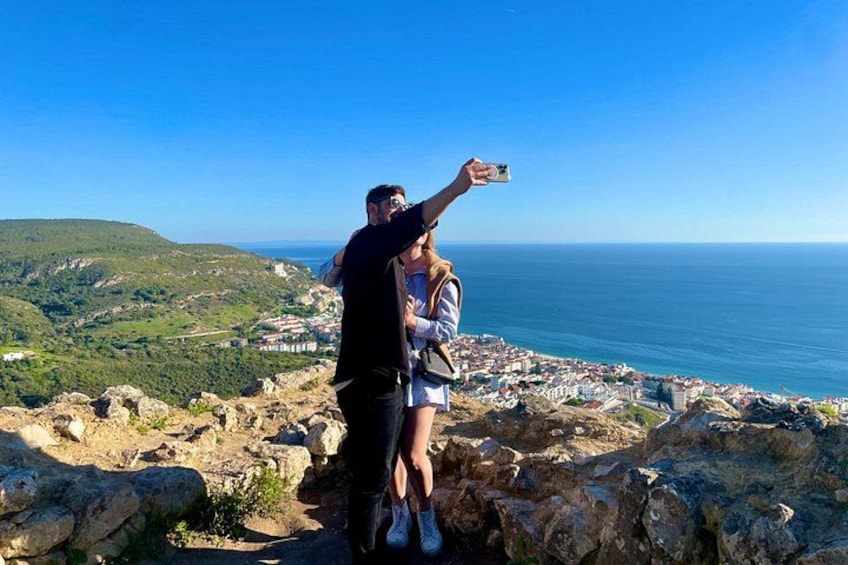 Una pareja se toma un selfie en un acantilado rocoso con vistas a un pueblo costero. 4