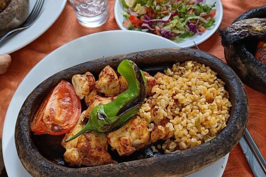 A meal with grilled chicken, rice, and vegetables served in a traditional clay bowl. 3