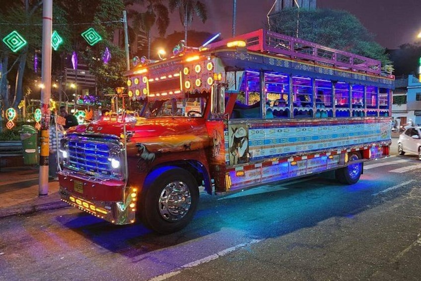 A brightly lit, colorful bus with intricate designs and lights, parked on a street at night. 1