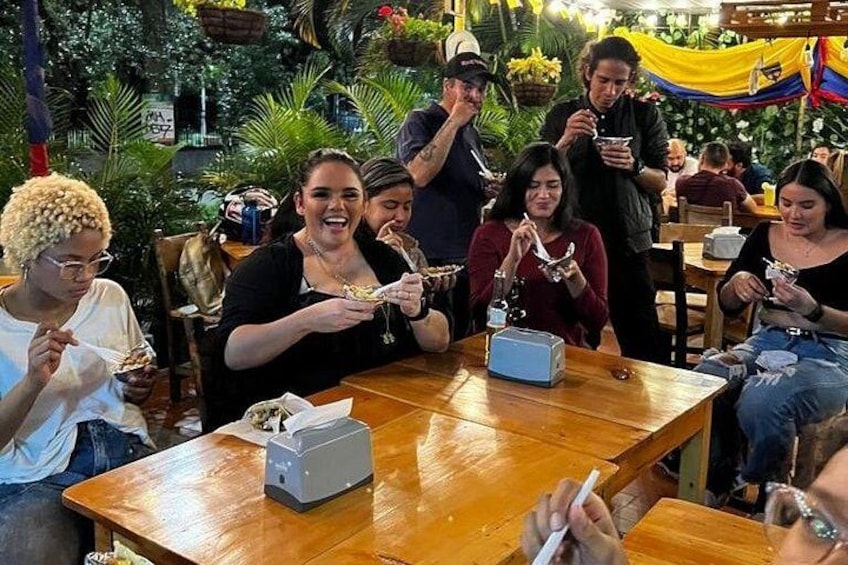 Un groupe de personnes est assis autour d’une table en bois dans un restaurant, avec des plantes tropicales en arrière-plan. 4