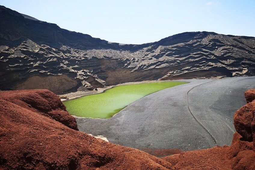 A dry lakebed with green water and red sand dunes. 1
