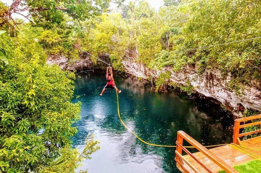 Una persona se balancea en una cuerda sobre un río, rodeada de vegetación y un puente de madera. 4