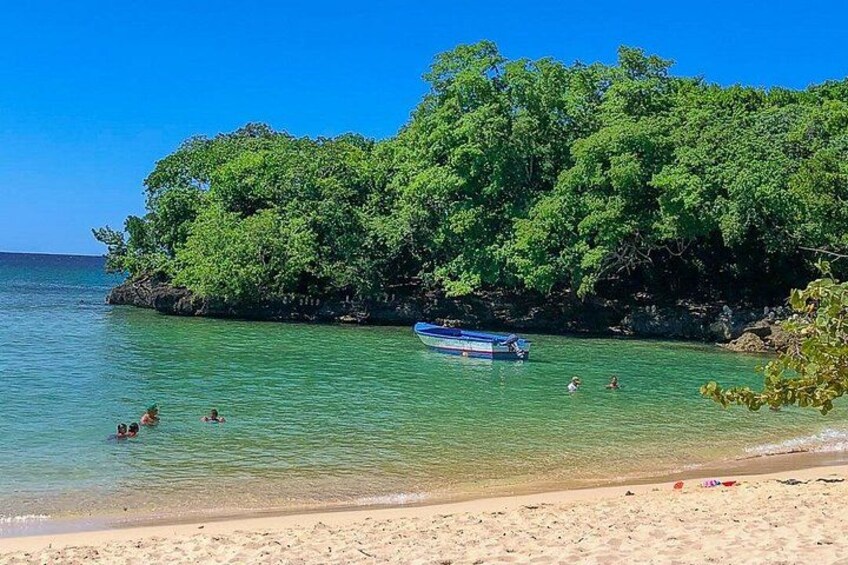 Una playa con agua turquesa cristalina, un bote pequeño y gente nadando. 5