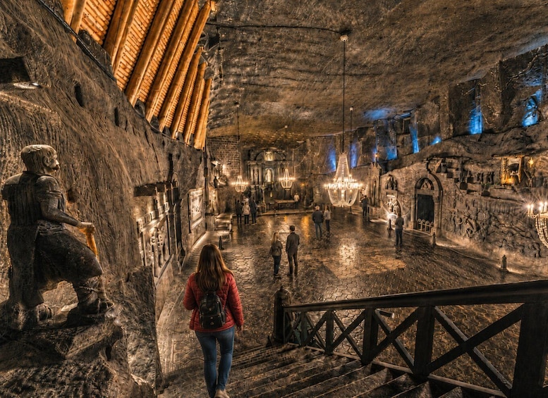 An indoor cave-like space with stone walls, a statue, and visitors. 4