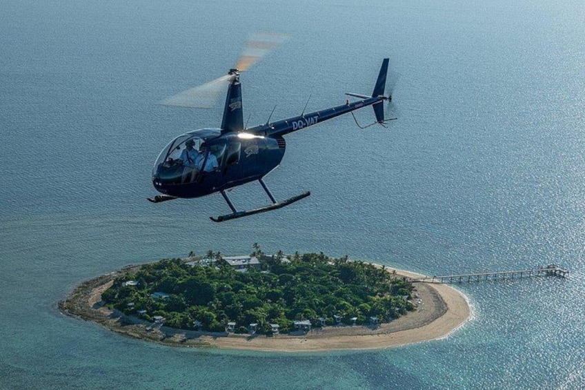 A helicopter flying over a small island with a beach and a pier. 1