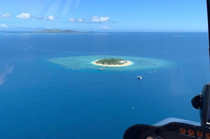 An aerial view of a turquoise island surrounded by deep blue ocean, with a clear sky above. 4