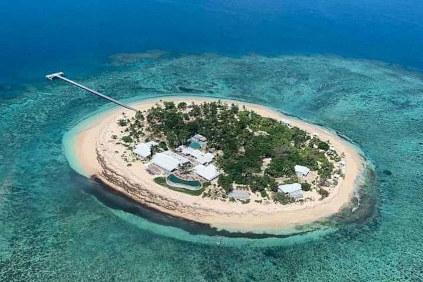 An aerial view of a small island with clear turquoise waters, a sandy beach, and a few buildings. 3