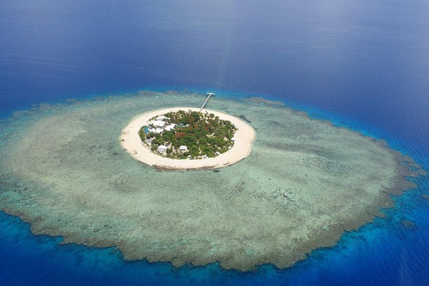An aerial view of a small island with a white sandy beach, surrounded by clear blue waters and a coral reef. 2