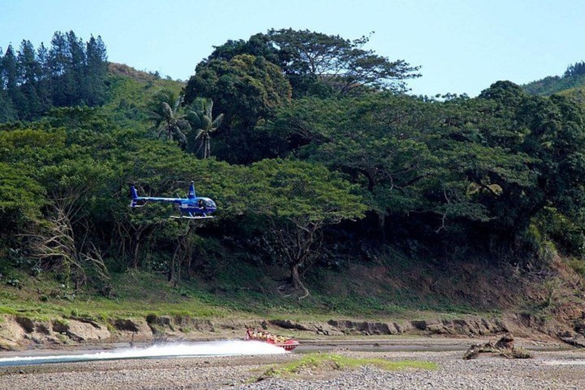 Ein Hubschrauber fliegt über eine Küstenregion mit dichter Vegetation und blauem Himmel. 1