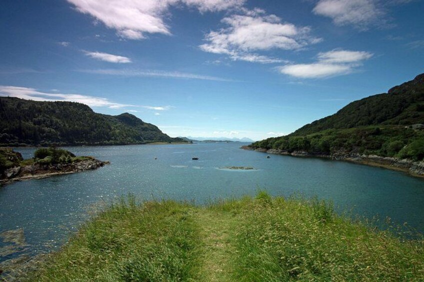 A calm lake surrounded by hills, a clear sky, and a boat in the distance. 2