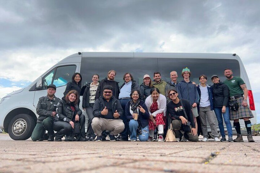 Un grupo de personas posando frente a una camioneta gris sobre una superficie pavimentada. 2