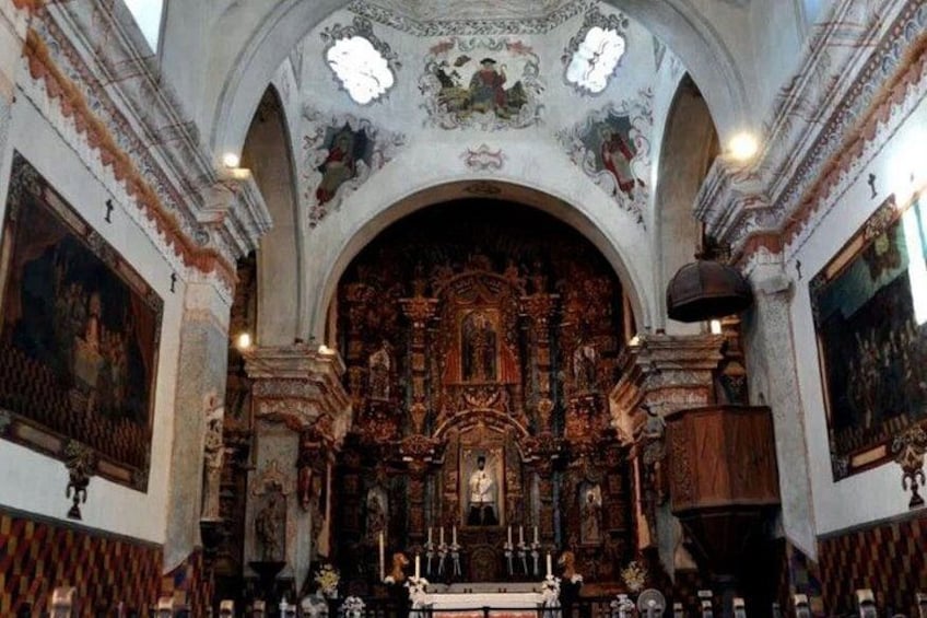Ein aufwändig gestaltetes Kircheninnere mit einem Hochaltar, detaillierten Fresken und einem großen Kruzifix. 2