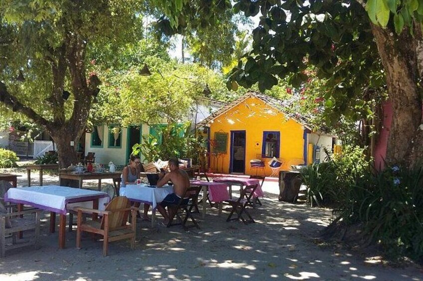 Ein Straßencafé mit Tischen und Stühlen, ein gelbes Gebäude und Bäume. 2
