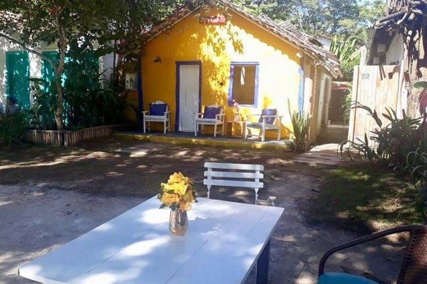 Ein gelbes Haus mit einer weißen Tür, einer weißen Bank und einem Tisch mit Blumen in einer Vase. 4