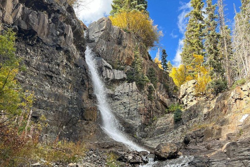 Een waterval die over een rotswand stroomt, omgeven door bomen met herfstkleuren. 4