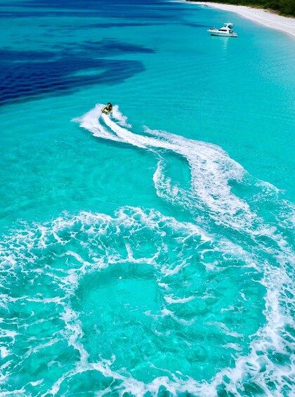 A boat creating a wake in turquoise waters with a sandy beach and a clear sky. 5