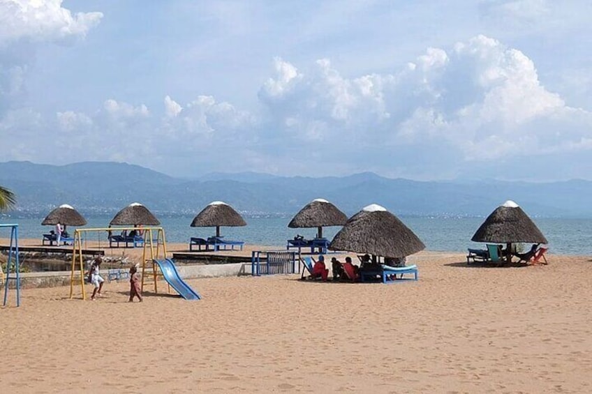 Een strand met rieten parasols, een speeltuin en mensen die ontspannen. 2