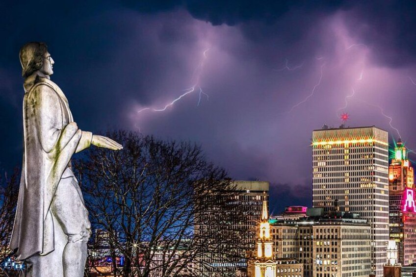 A statue, a cityscape with buildings, and lightning in the sky. 4