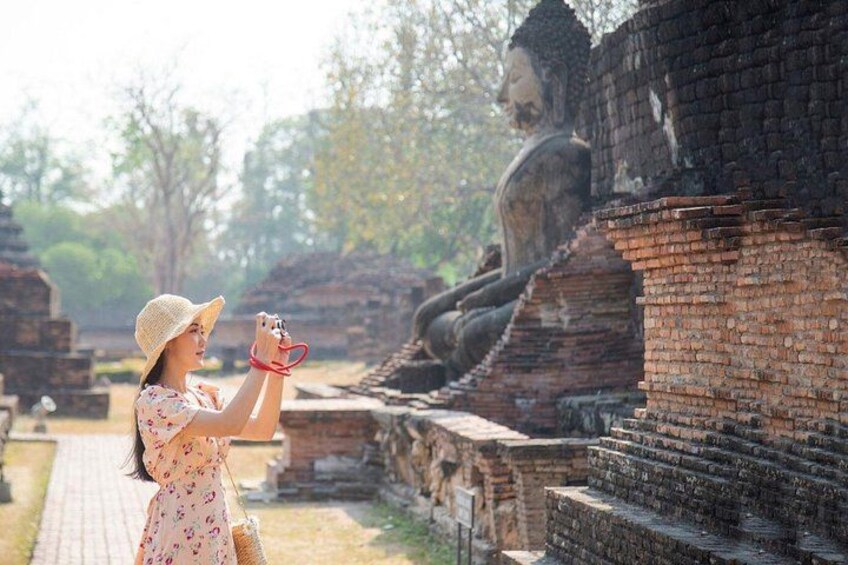 A person taking a photo of a large seated Buddha statue in an ancient temple complex. 3