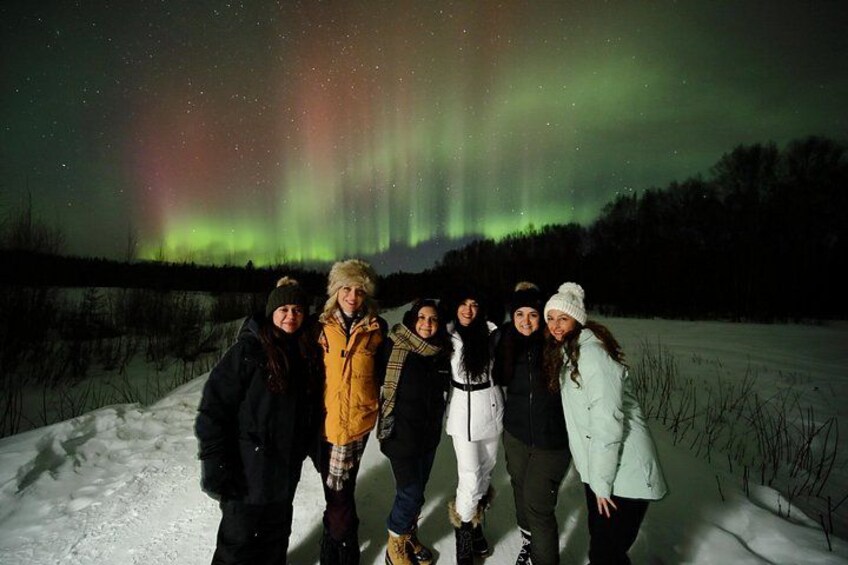 A group of people standing in a snowy field with the Northern Lights in the background. 2