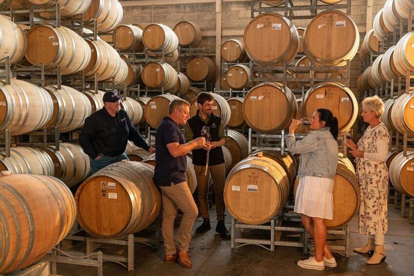 A group of people inspecting large wooden barrels in a warehouse. 1
