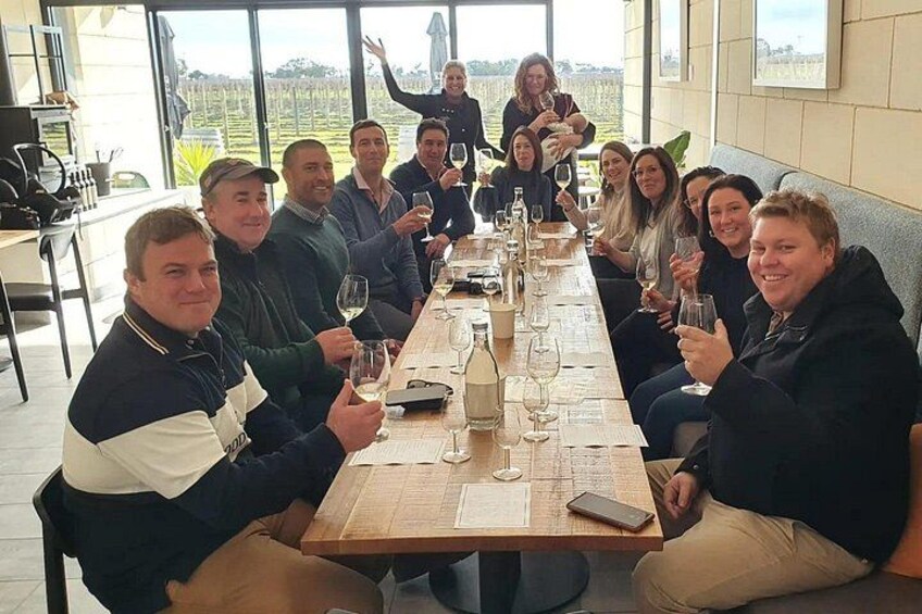A group of people seated at a long table with wine glasses, in a room with large windows. 4