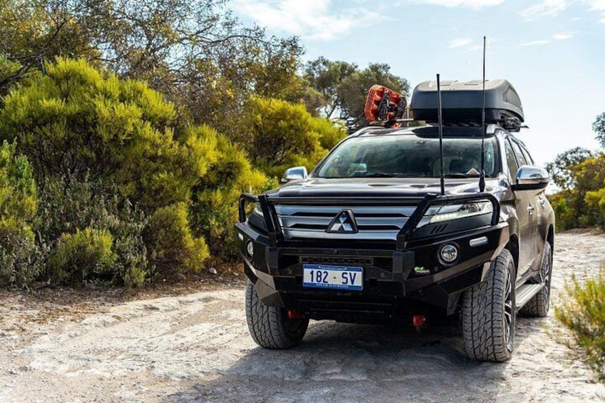 A black SUV with a roof rack and a license plate on a dirt road surrounded by greenery. 5