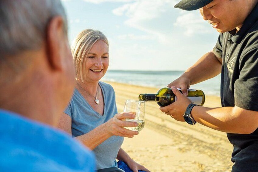 A person pouring a drink into a glass on a beach. 3