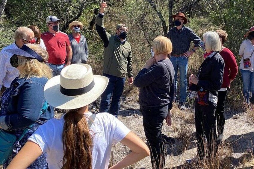 Un grupo de personas al aire libre, algunas de pie y otras sentadas, en un entorno natural con árboles y hierba seca. 5