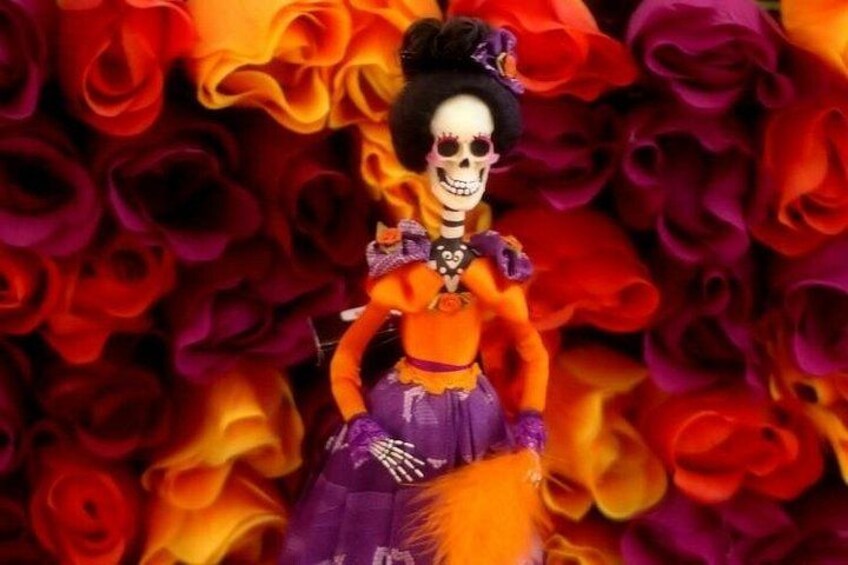 Una figura esquelética con un atuendo vibrante naranja y morado, sobre un fondo floral. 4