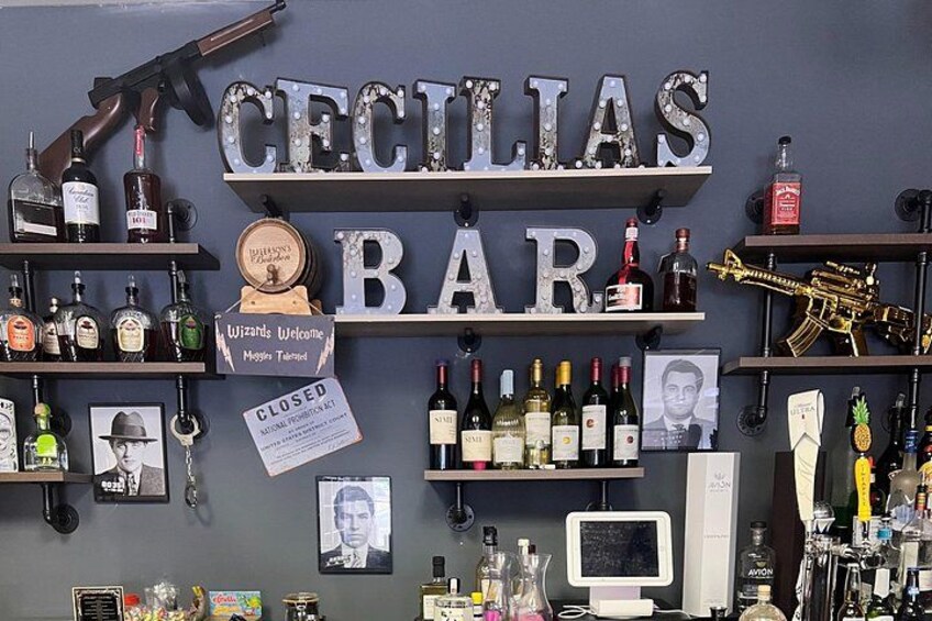 A bar named 'Cecilia's Bar' with shelves of liquor bottles, a sign welcoming visitors, and a closed sign. 1
