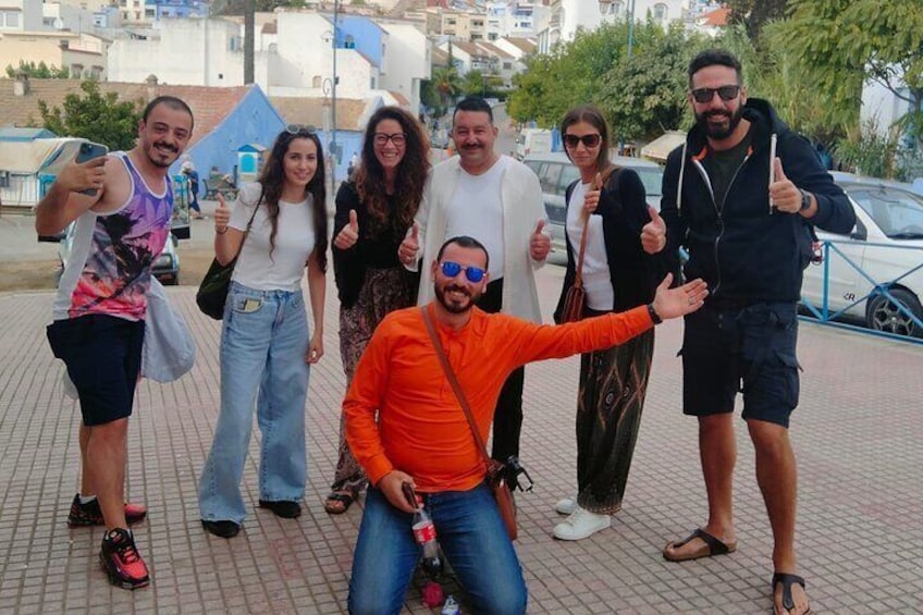 A group of people posing for a photo on a paved area with buildings and trees in the background. 1