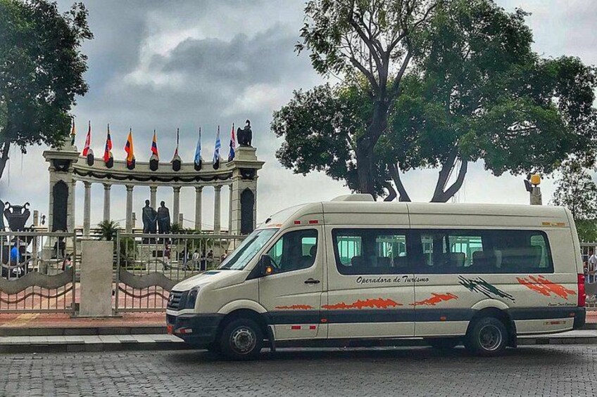 Un fourgon blanc est garé devant un monument, avec plusieurs drapeaux, une clôture et des arbres en arrière-plan. 1