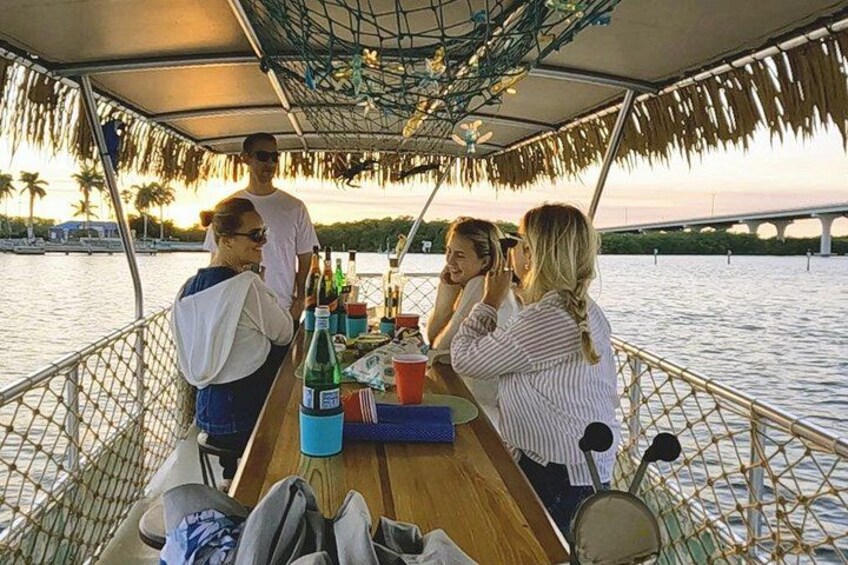 Un grupo de personas en un barco con una mesa de bebidas y un toldo de malla por encima. 1