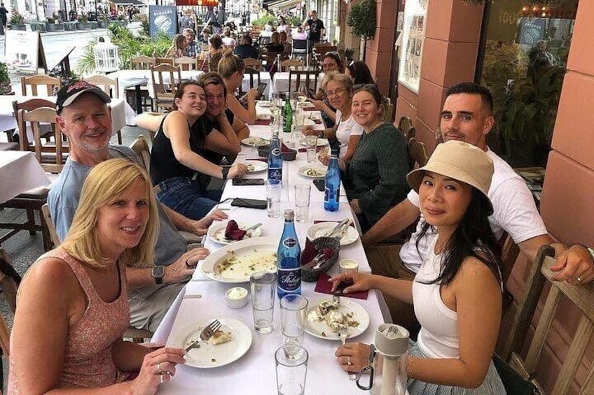 Un groupe de personnes est assis à une table dans un restaurant en plein air, où se trouvent également des chaises. 1