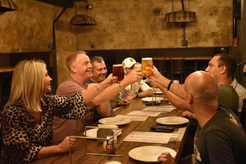 A group of people toasting with drinks at a wooden table in a rustic setting. 1