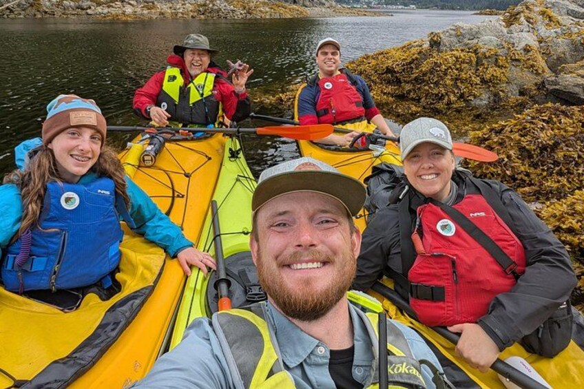 A group of people in a yellow kayak on a calm river surrounded by rocks and vegetation. 3