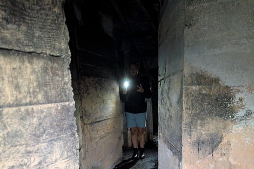 A person standing in a dimly lit, narrow passageway with rough, aged walls. 5