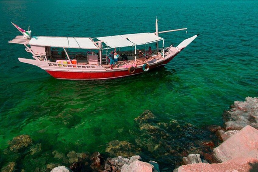 A red boat with a white canopy, floating on clear turquoise water near rocky shores. 2