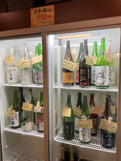Una vetrina refrigerata con diverse bottiglie di liquori giapponesi, ognuna con un'etichetta di prezzo. 2