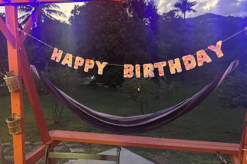 A hammock with 'HAPPY BIRTHDAY' decorations, set against a backdrop of trees and hills. 3