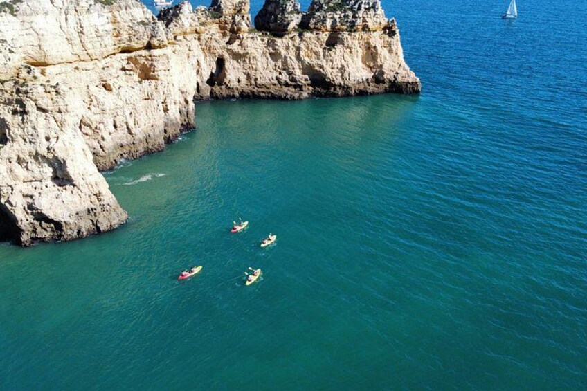 Zona costera con acantilados rocosos y agua turquesa cristalina. Varias kayaks sobre el agua. 3