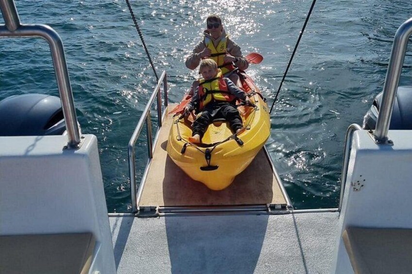 Un kayak amarillo sobre la cubierta de un barco, con dos personas usando chalecos salvavidas. 5