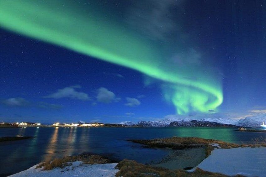 Nattebillede med nordlys over et roligt vand og sneklædte bjerge. 4