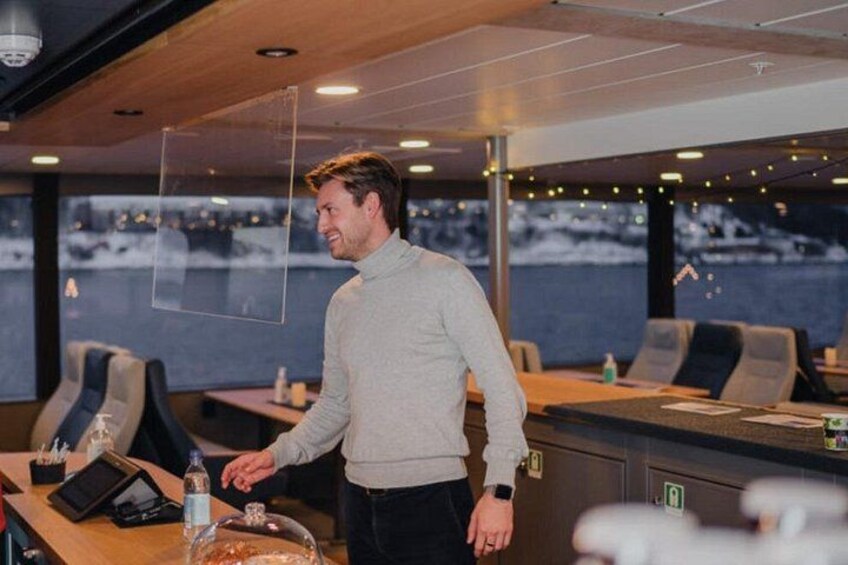 En mand i en afslappet sweater står i et moderne, veloplyst rum med et stort vindue med udsigt over et sneklædt landskab. 2