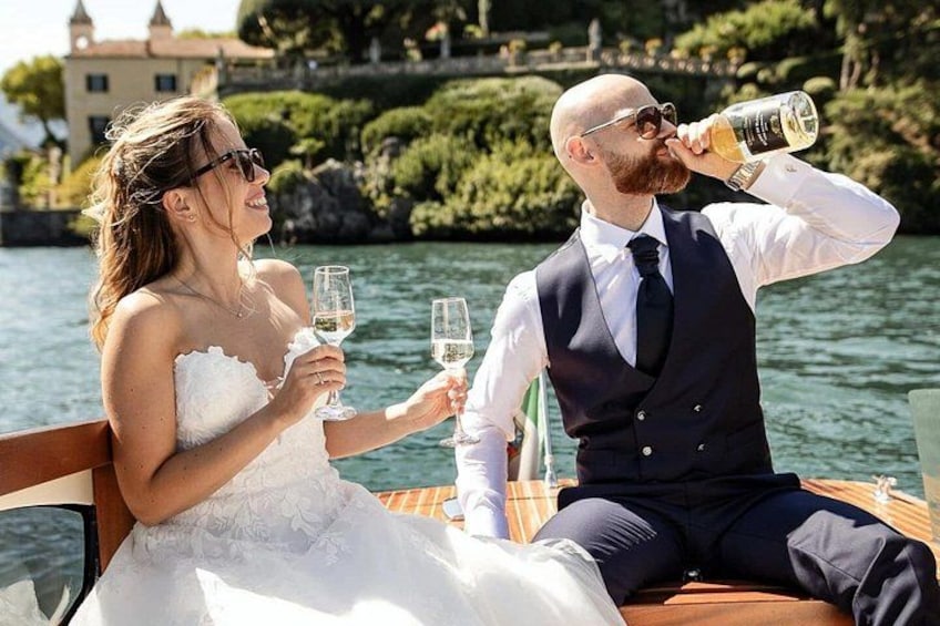 Un couple de jeunes mariés sur un bateau, avec une étendue d’eau et un bâtiment en arrière-plan. 2
